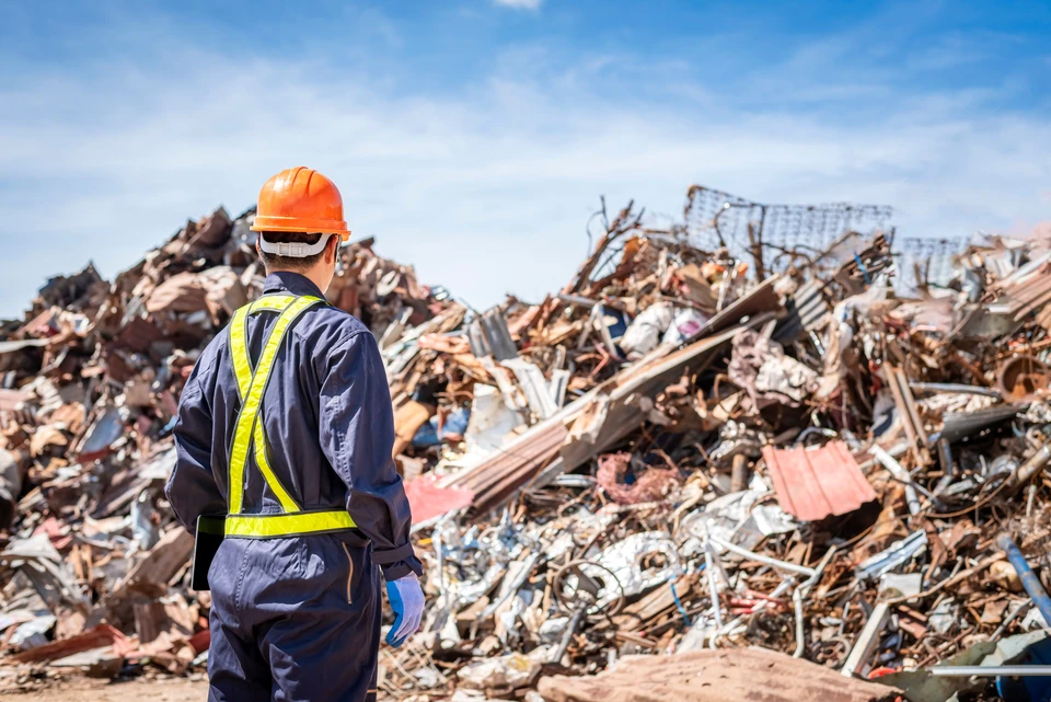 Ouvrier en équipement de protection individuelle avec casque orange et gilet haute visibilité jaune observant un site de démolition ou décharge de matériaux de construction