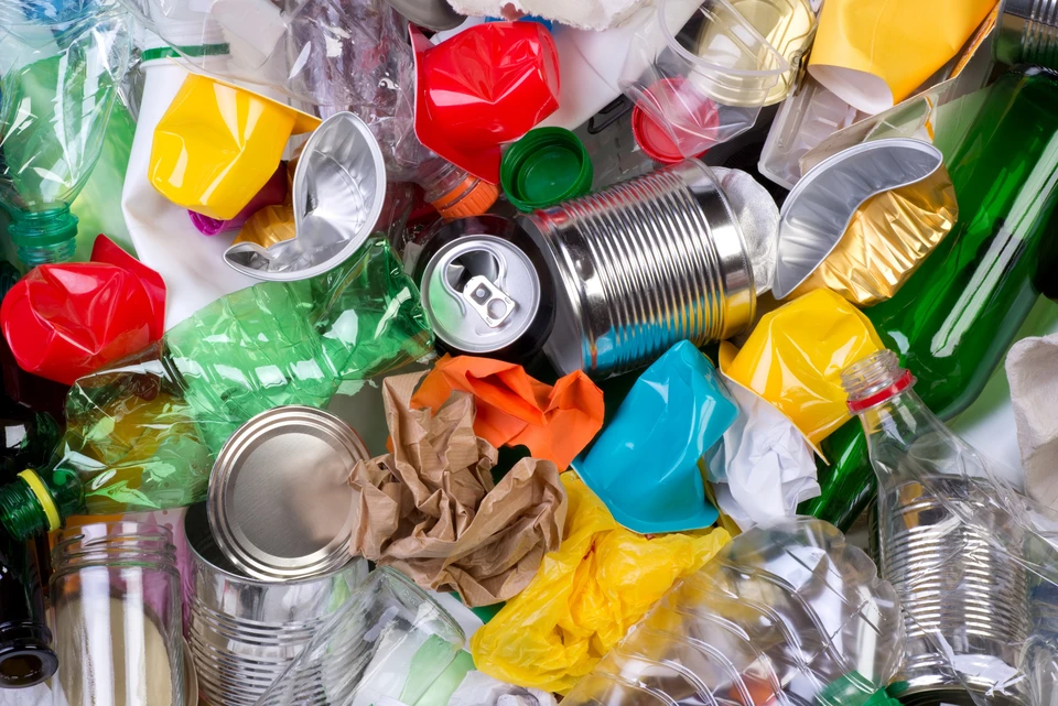 Amas de déchets recyclables mélangés : bouteilles plastique vertes et transparentes, canettes aluminium, boîtes de conserve métalliques, emballages colorés froissés, contenants divers jetés en vrac