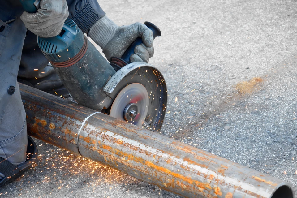 Chantier de construction extérieur avec ouvrier en casque de sécurité orange et t-shirt rouge manipulant une scie circulaire électrique portative sur poutre en bois lamellé-collé
